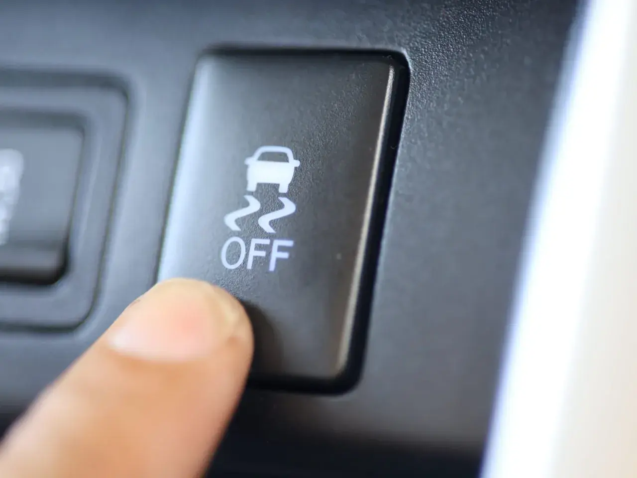 Dedo presionando el botón "OFF" del control de tracción, con el icono de un coche derrapando.