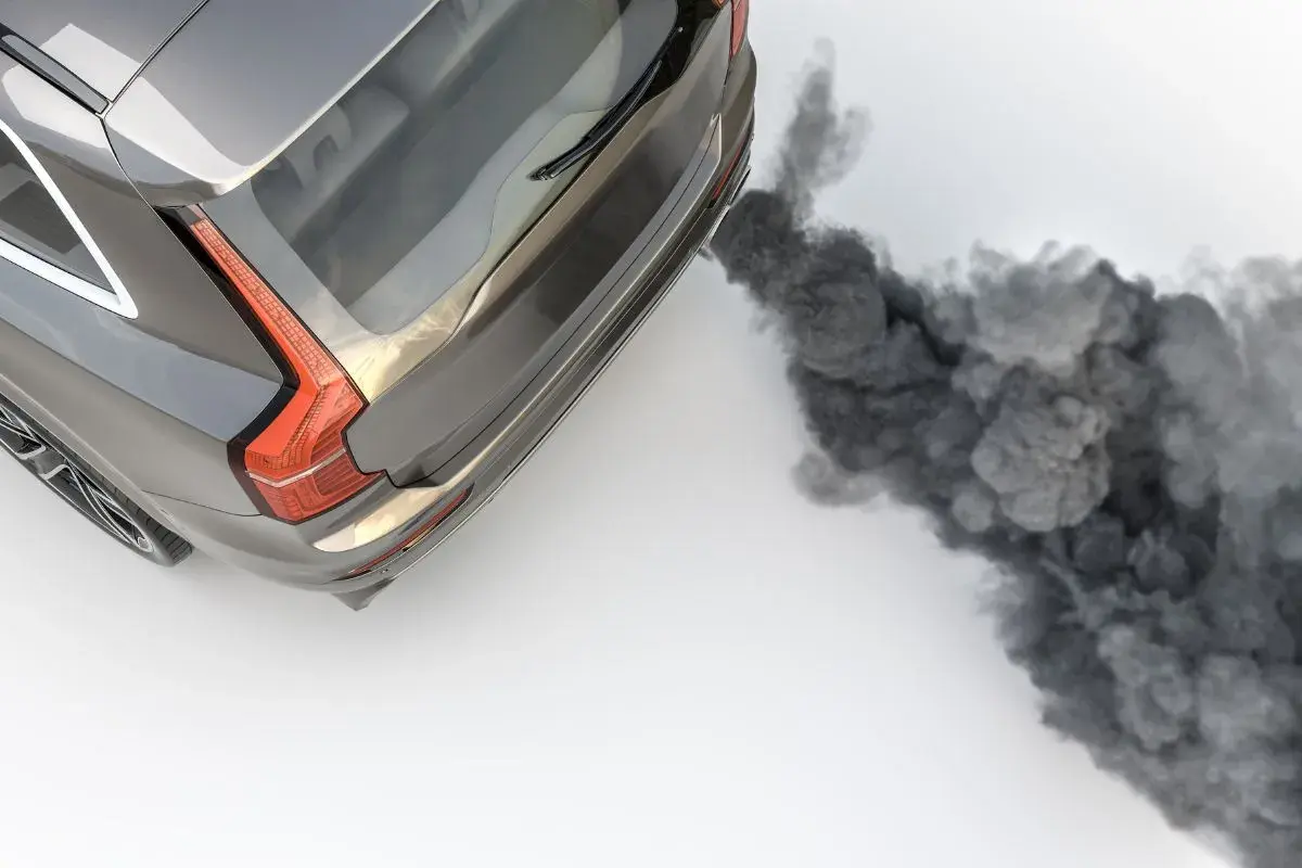 Un coche emite una densa nube de humo negro por el tubo de escape al acelerar, contaminando el aire.
