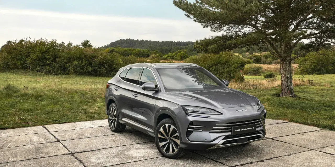 Un SUV gris moderno, uno de los coches híbridos autorrecargables, descansa sobre una plataforma de hormigón en un paisaje natural.