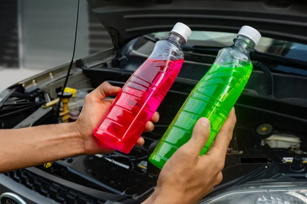 Manos sostienen botellas con líquido refrigerante de colores, rosa y verde, para el agua de motor coche.