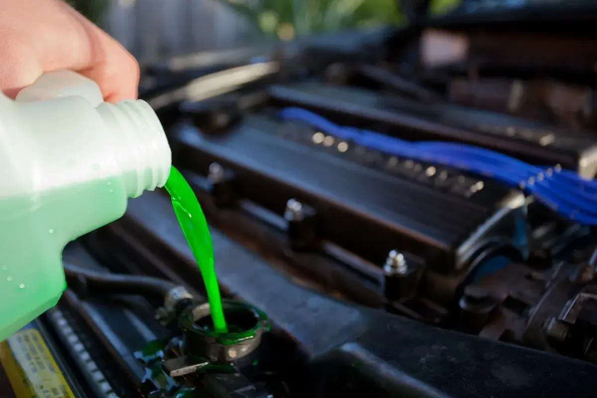 Vertiendo líquido refrigerante verde brillante en el radiador de un coche. El nivel líquido refrigerante es crucial para el motor.