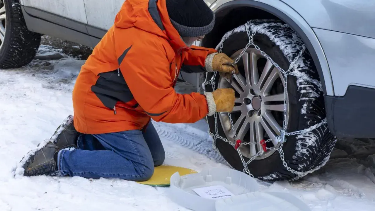 Persona con guantes ajusta la cadena del coche a la rueda cubierta de nieve.