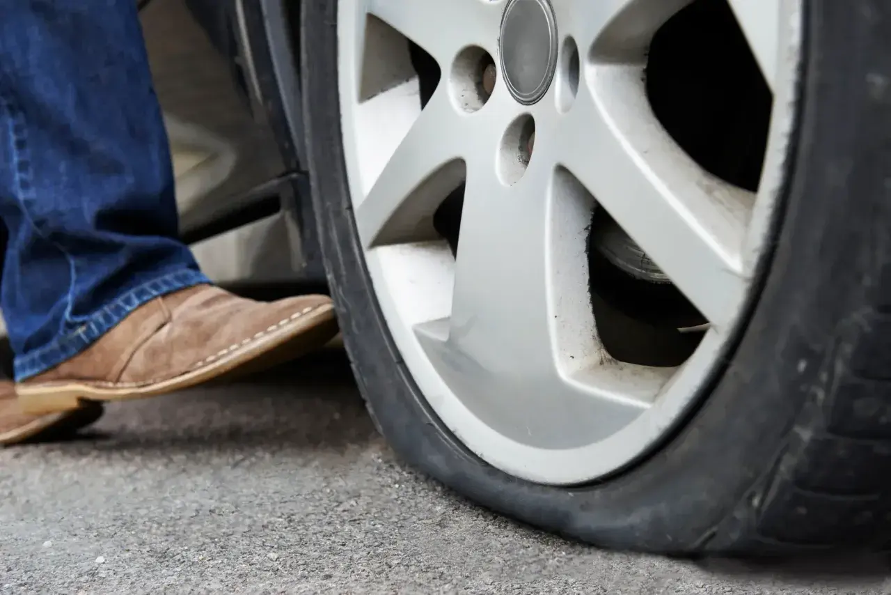 Un neumático pinchado, ¿qué es un runflat? Un pie con zapato de gamuza se acerca a la rueda desinflada.