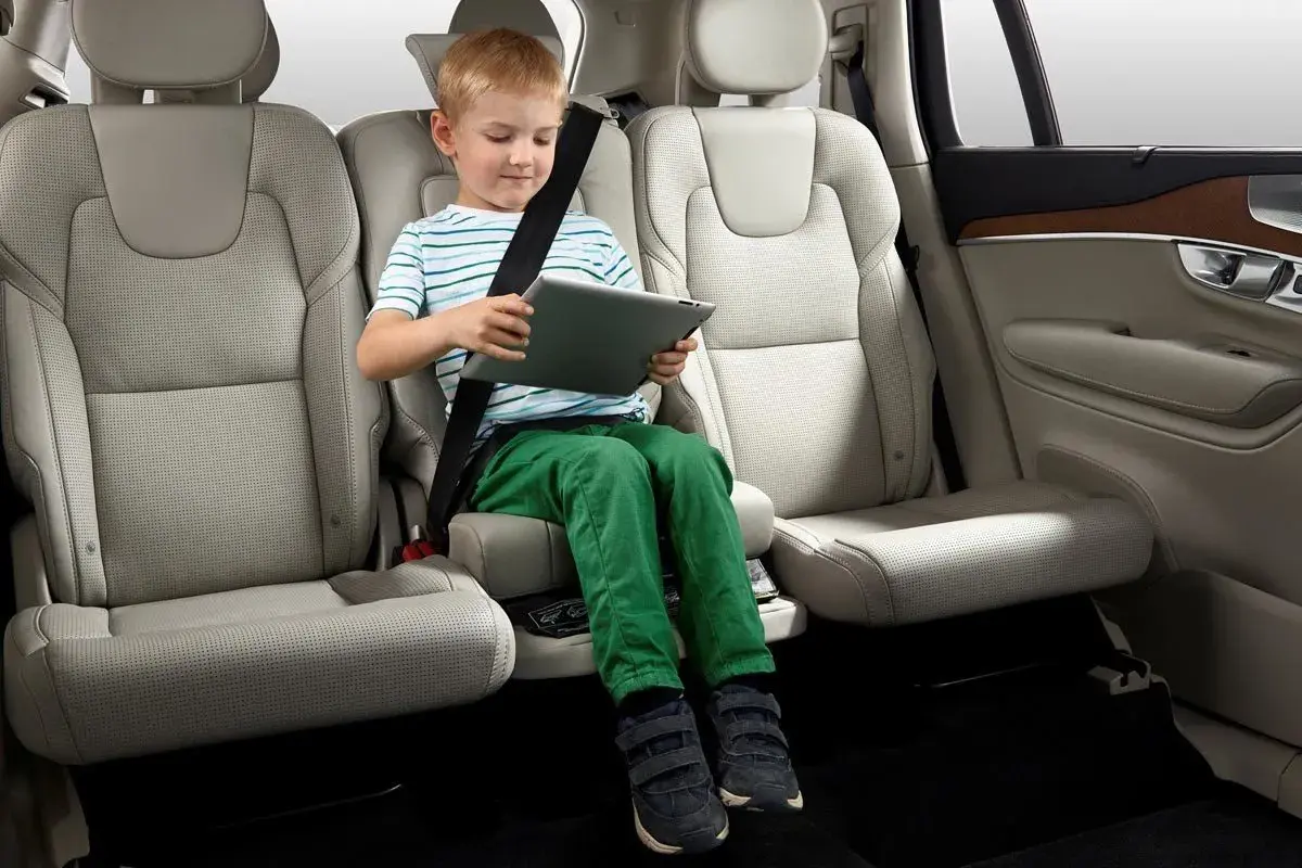 Niño sentado en asiento elevador integrado en el coche, entretenido con una tablet. Ideal para saber donde poner silla bebe coche.
