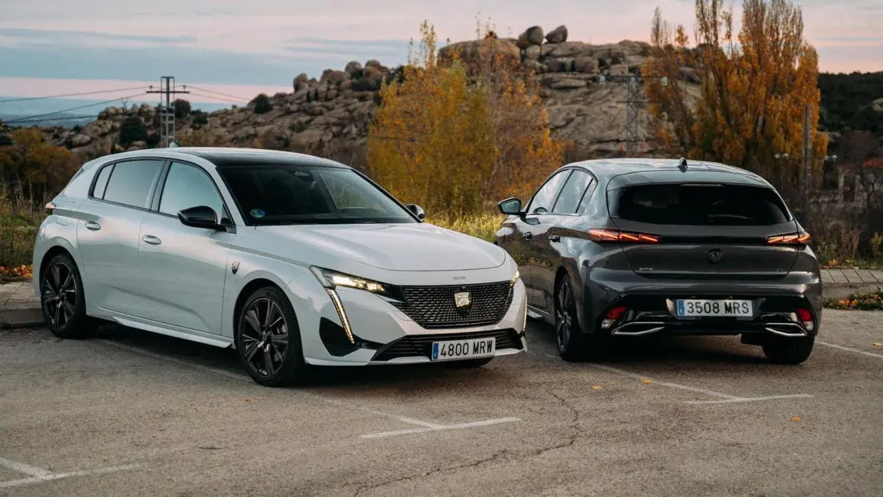 Dos Peugeot 308, uno blanco y otro gris oscuro, aparcados al aire libre. Los coches híbridos son diésel o gasolina, ofreciendo opciones eficientes.