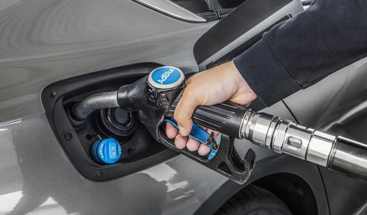 Persona rellena el depósito de AdBlue de un coche. Saber cuanto AdBlue consume un coche es clave para planificar repostajes.