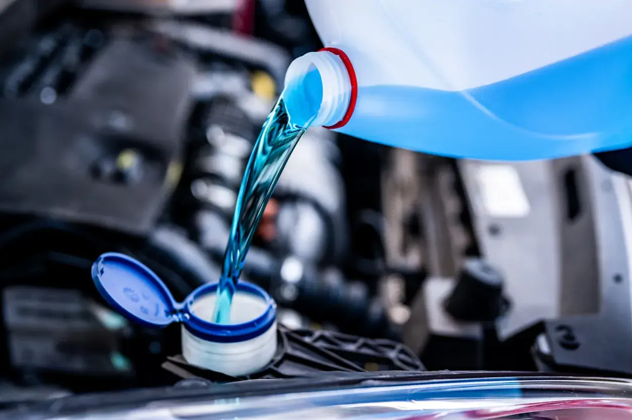 Líquido azul brillante se vierte de una botella a un depósito del coche. Es hora de decidir qué anticongelante usar para proteger tu motor.