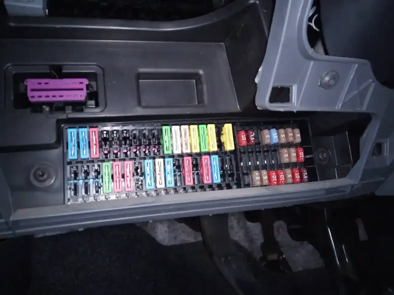 Panel de fusibles de un Seat Ibiza 6J con varios fusibles de colores y un conector púrpura.