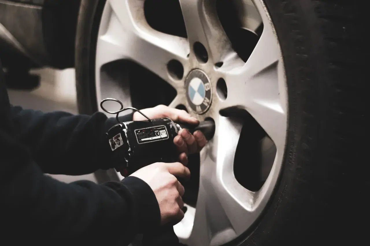Mano usando una llave de impacto para cambiar ruedas delanteras por traseras en un coche BMW.