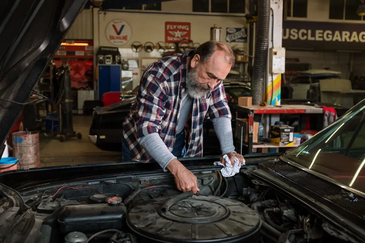 Mecánico revisa el motor de un coche clásico, buscando la causa por la que no salta el ventilador del coche.