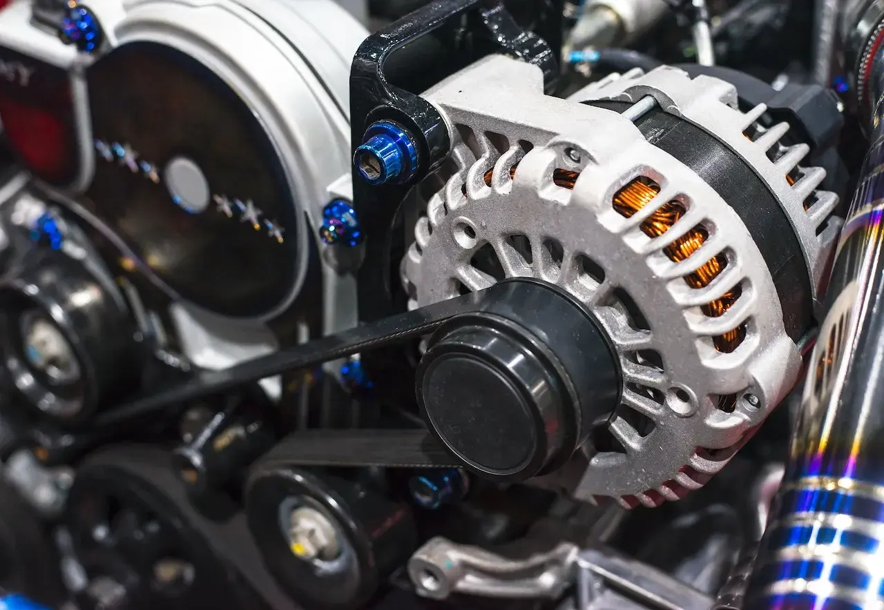 El alternador de un coche, con su polea y correa, genera electricidad. Se ve el motor y sus componentes.
