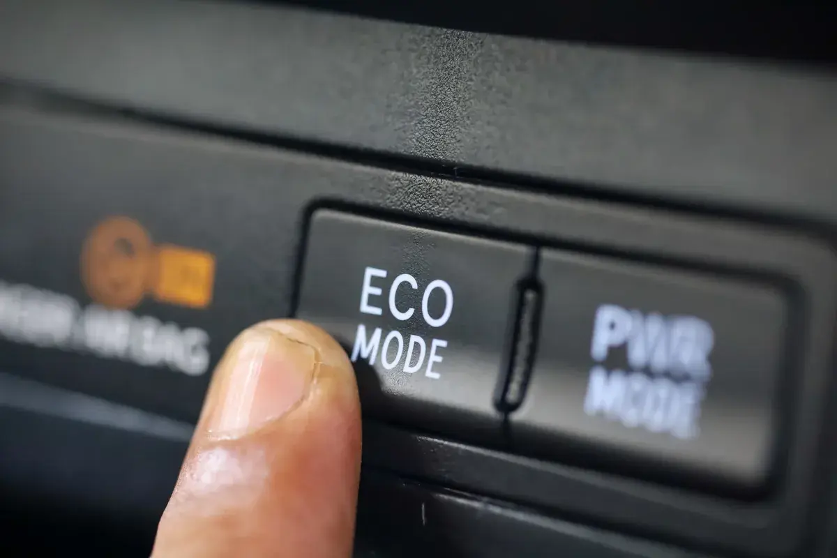 Dedo presionando el botón "ECO MODE" en un coche, optimizando el consumo de gasolina para viajes más eficientes.