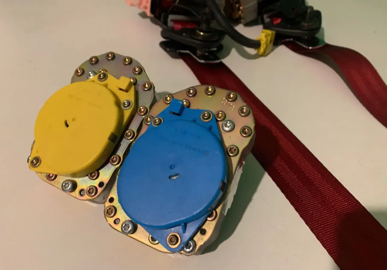Mecanismo de cinturón de seguridad con carretes amarillo y azul, listo para reparar cinturón de seguridad deshilachado.