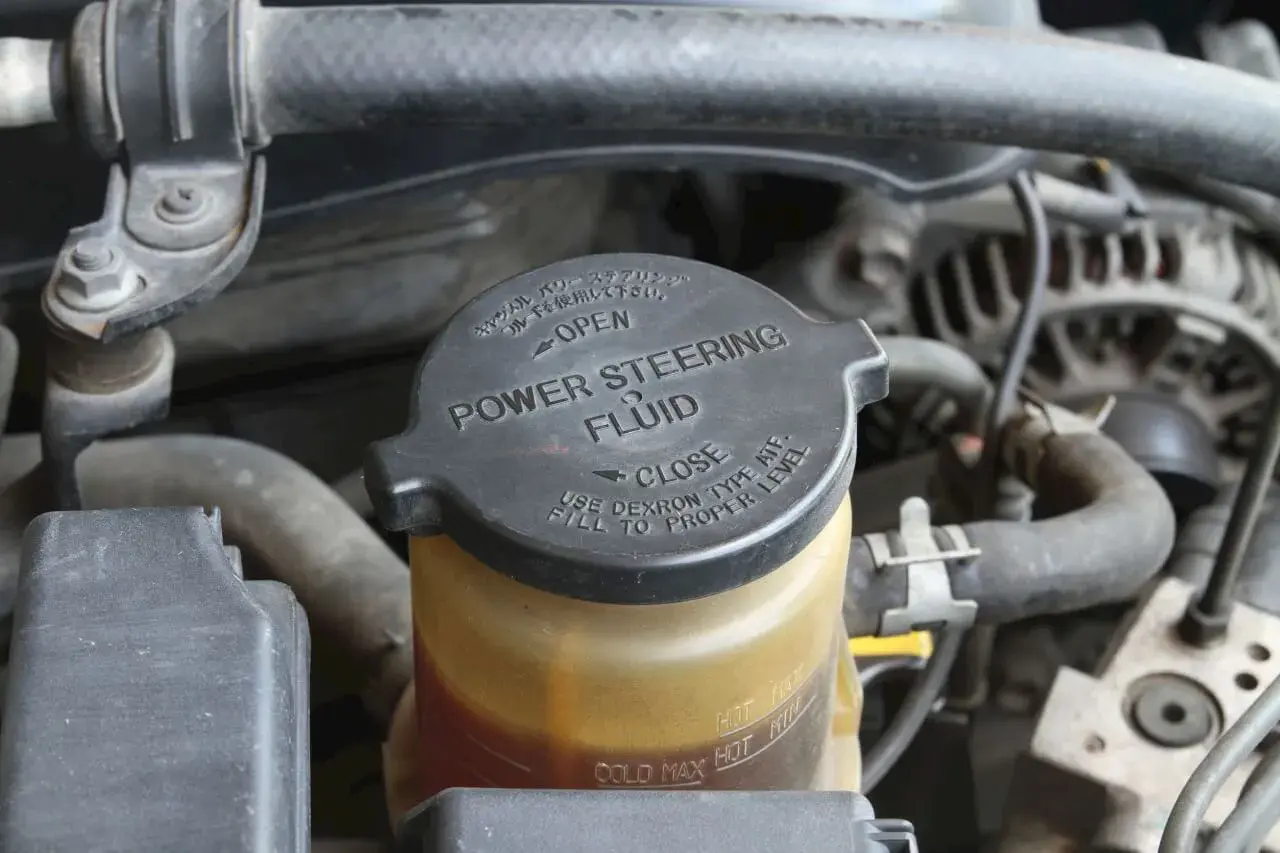 Depósito de líquido de dirección asistida. La tapa negra indica "POWER STEERING FLUID" y las marcas de nivel.