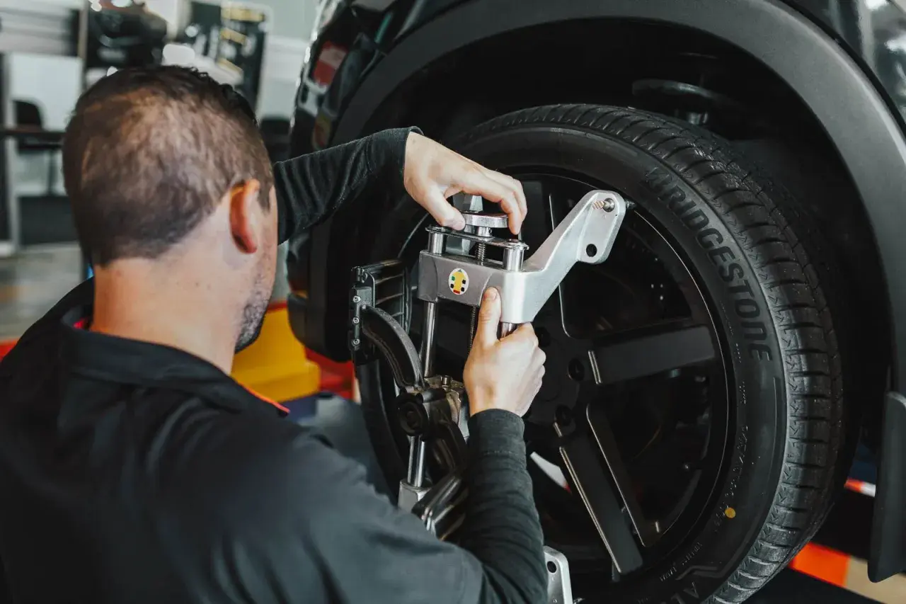 Mecánico ajusta un sensor en la rueda de un coche. Averigua cuanto cuesta alinear un coche para un manejo seguro.