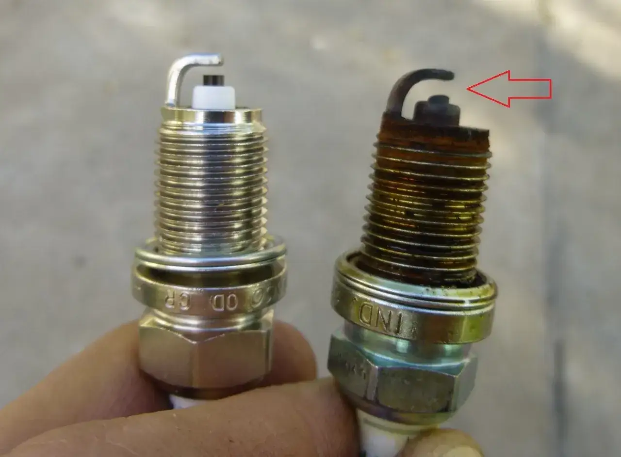 Una bujía nueva y otra desgastada, con óxido y el electrodo doblado, muestran cómo saber si las bujías están mal.
