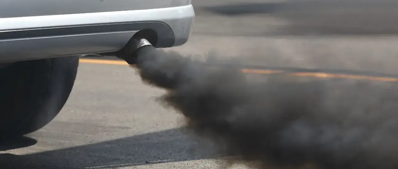 Un coche emite humo negro por el tubo de escape al acelerar, contaminando el aire.