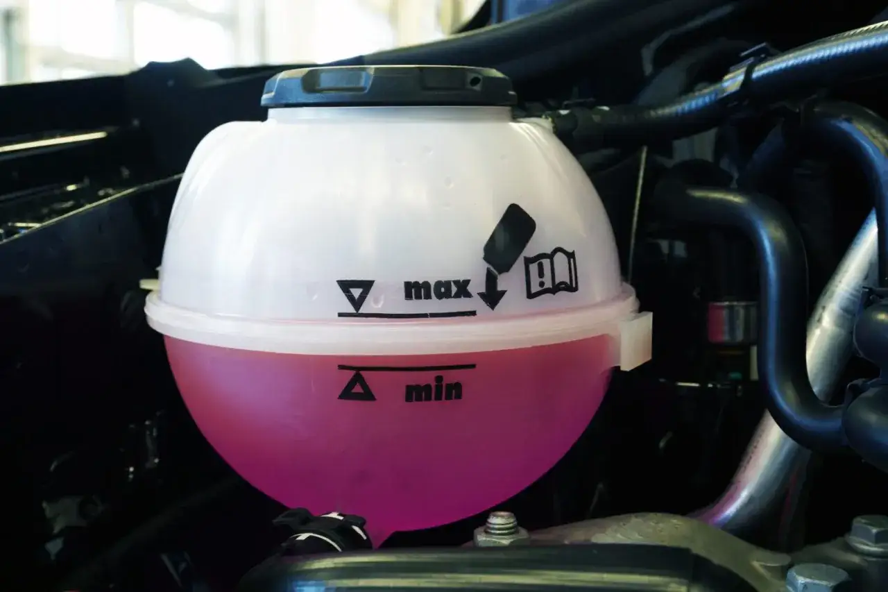 Depósito de expansión con líquido refrigerante rosa. El nivel de agua del radiador del coche está entre las marcas 
