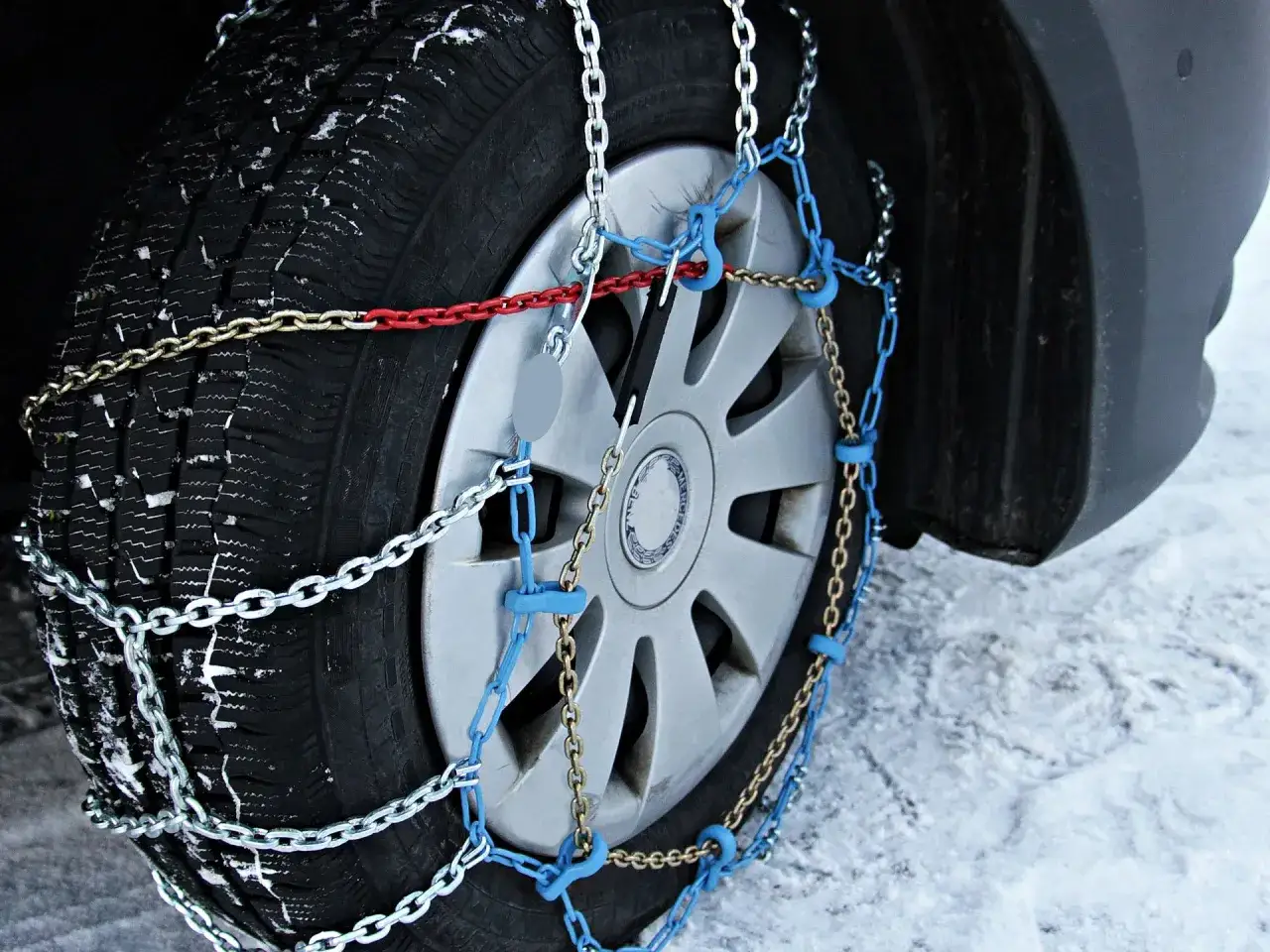Neumático de coche cubierto de nieve con una cadena del coche instalada para mejorar la tracción en condiciones invernales.