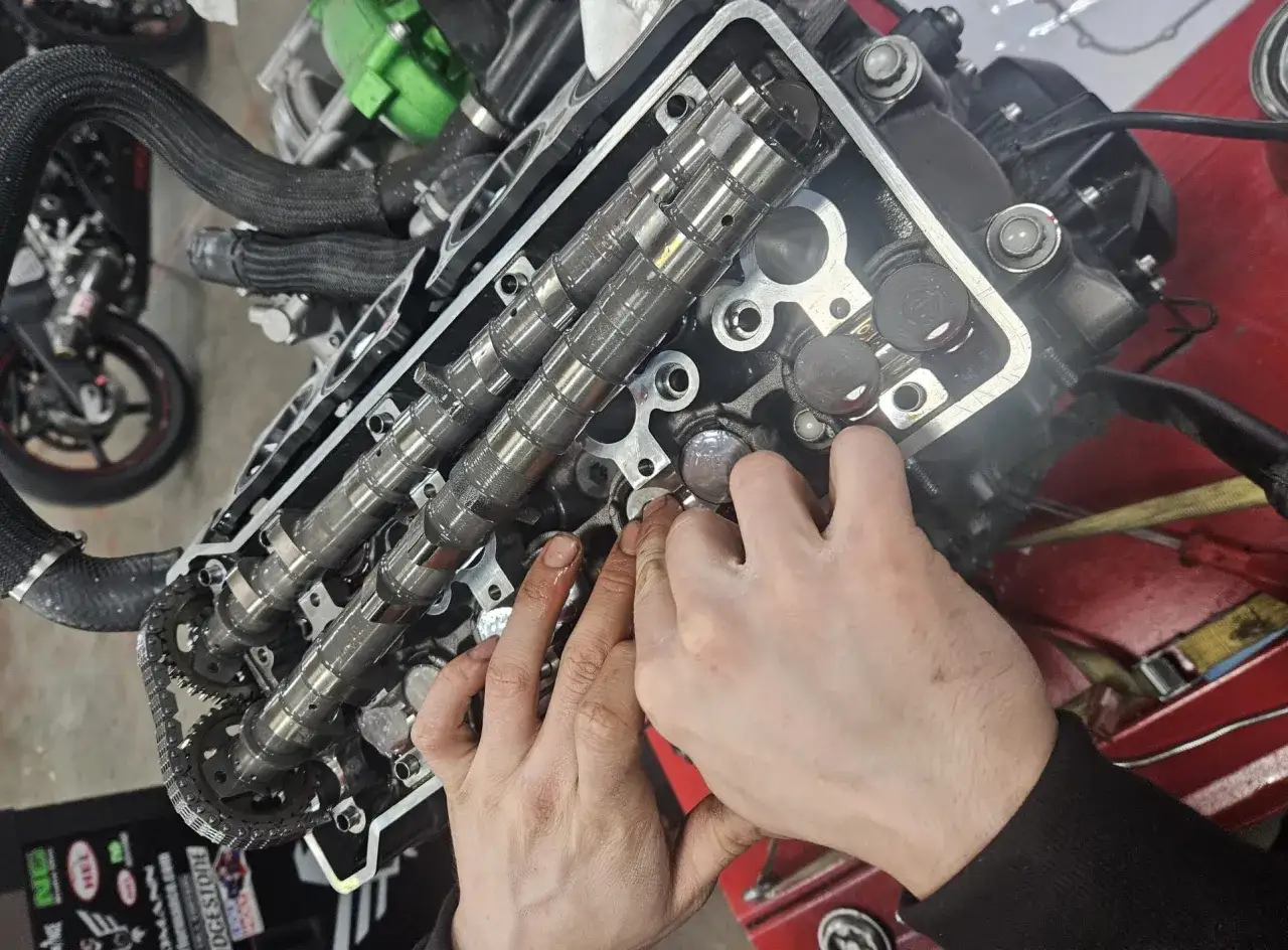 Mecánico revisa el motor de una moto, buscando señales de cómo saber si la culata está dañada. Se aprecian válvulas y árbol de levas.