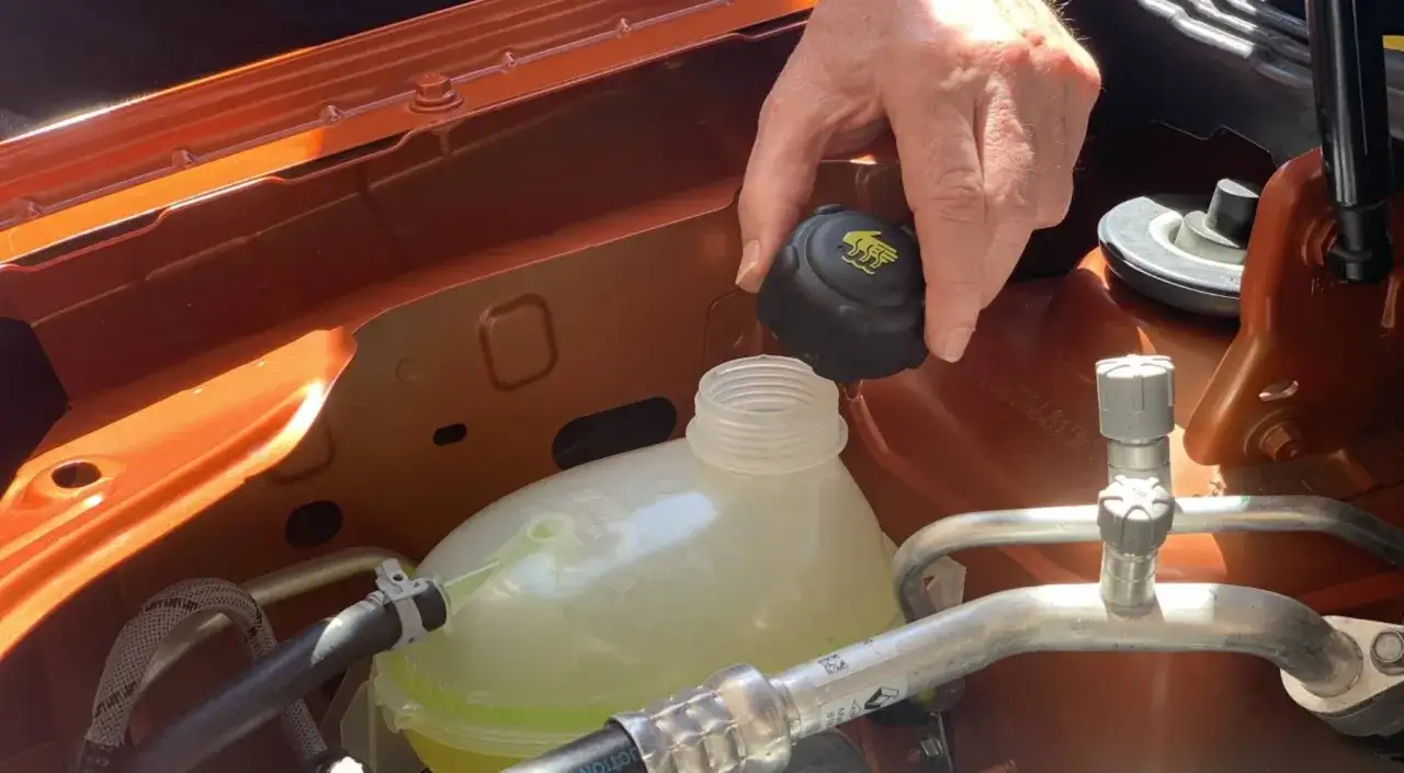 Mano retirando tapa del depósito de refrigerante. Revisa cada cuanto se cambia el líquido refrigerante para el buen funcionamiento del motor.