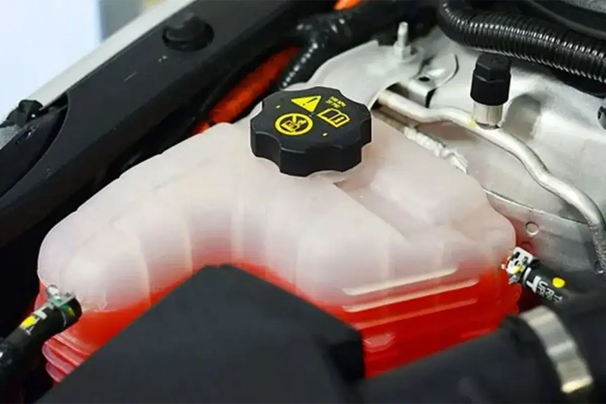 Depósito de agua de motor coche con líquido refrigerante rojo. Tapa negra con símbolos de advertencia.