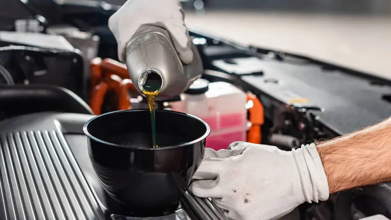 Mano enguantada vierte aceite de coche nuevo en un embudo. Es importante cambiarlo antes de que el aceite de coche caduca.