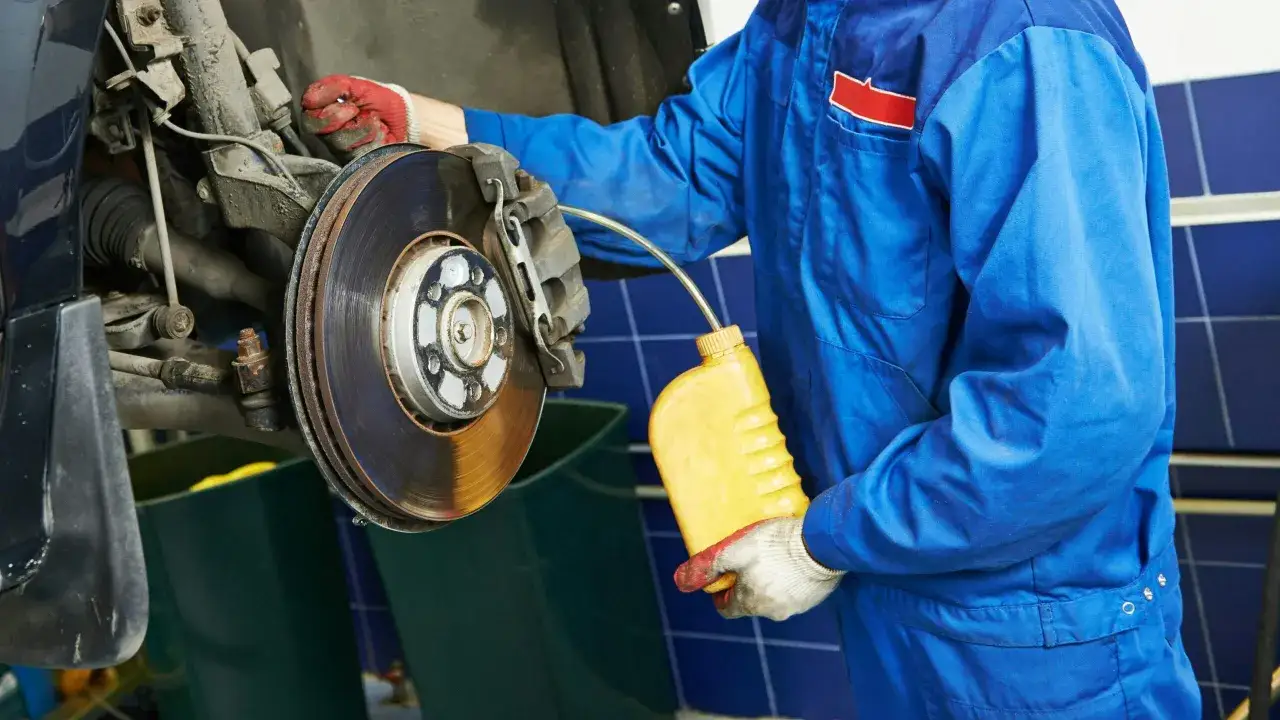 Mec&aacute;nico en uniforme azul realiza el cambio l&iacute;quido frenos de un coche, sosteniendo una botella amarilla.