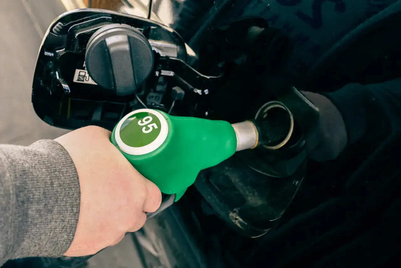 Mano sujetando una manguera de gasolina verde con el número 95 en un círculo verde. El coche se está repostando. Sin plomo 95 es gasolina.