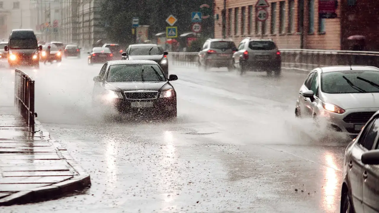 Coches circulando con lluvia intensa, levantando grandes salpicaduras de agua en la carretera mojada.