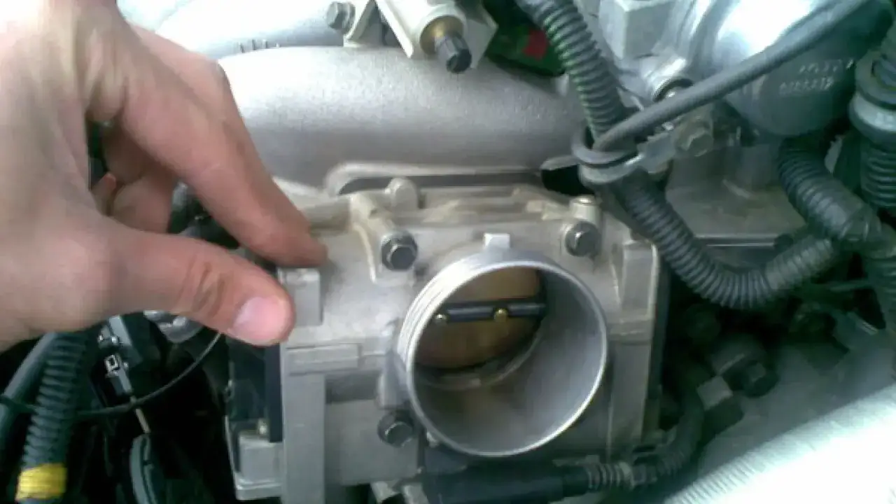 Mano ajustando la válvula mariposa coche, parte del sistema de admisión de aire del motor.