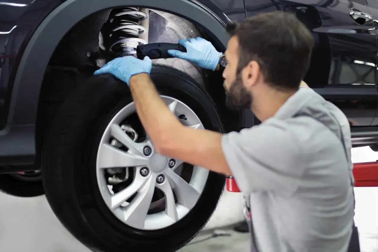 Mecánico con guantes azules revisa el amortiguador delantero de un coche.