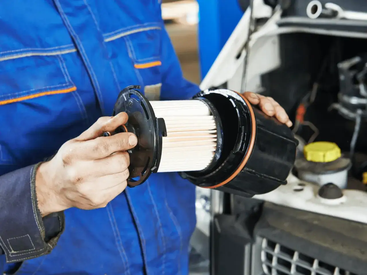 Mec&aacute;nico con mono azul muestra un filtro de combustible nuevo, listo para instalar y mantener el motor limpio.