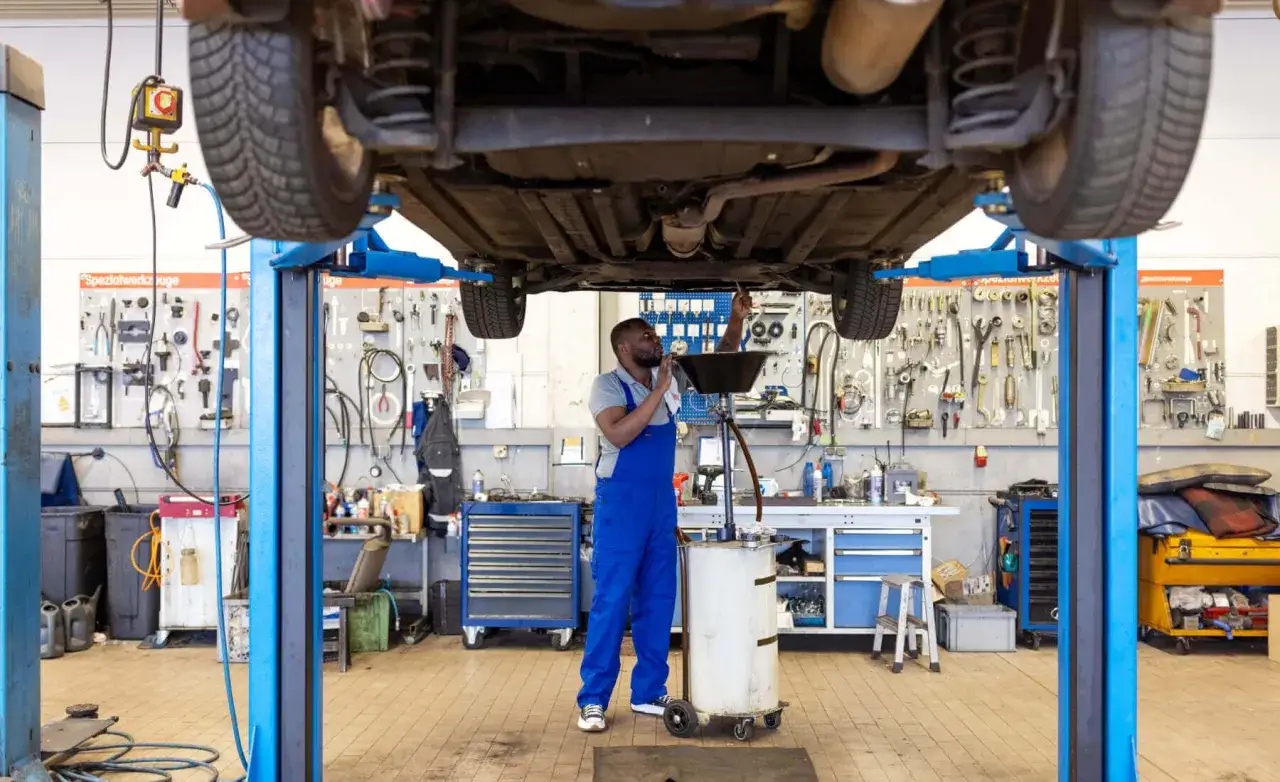 Mecánico realizando cambio de aceite a un coche elevado. Aprende como cambiar el aceite del coche sin elevador con esta guía visual.